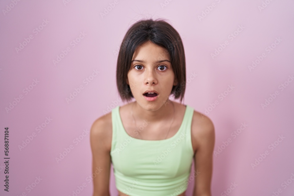 Young girl standing over pink background afraid and shocked with surprise and amazed expression, fear and excited face. Young girl standing over pink background afraid and shocked with surprise and amazed expression, fear and excited face.