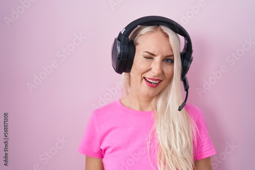 Caucasian woman listening to music using headphones winking looking at the camera with sexy expression, cheerful and happy face.