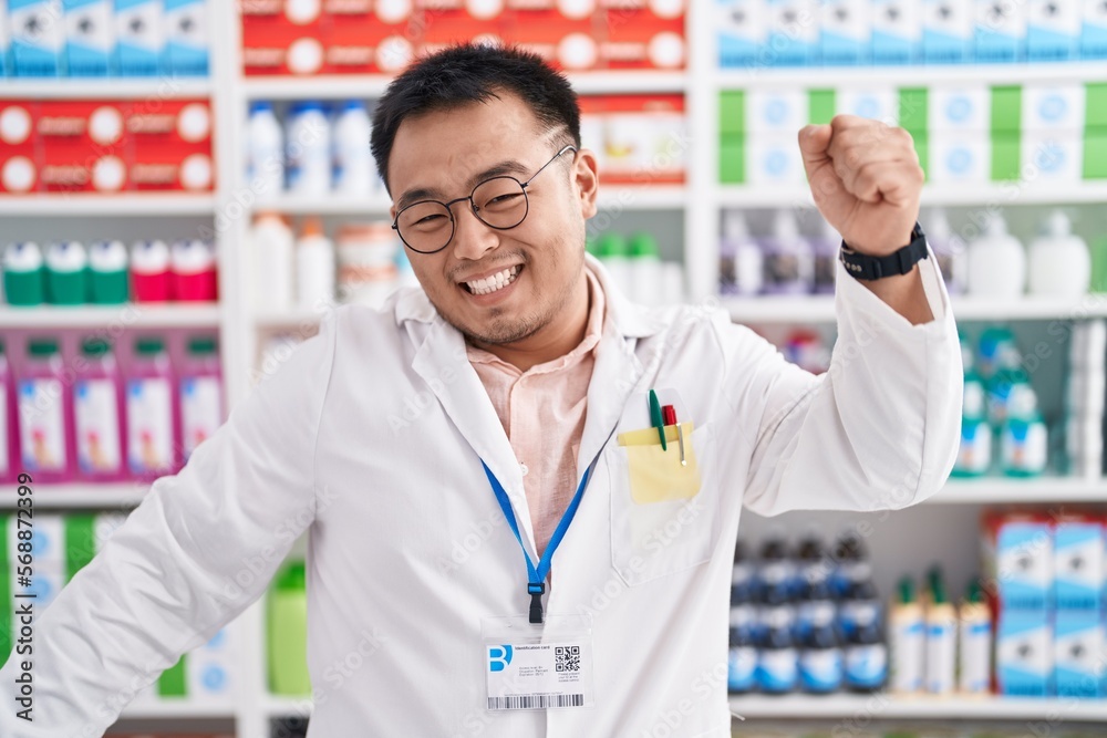 Chinese young man working at pharmacy drugstore dancing happy and cheerful, smiling moving casual and confident listening to music