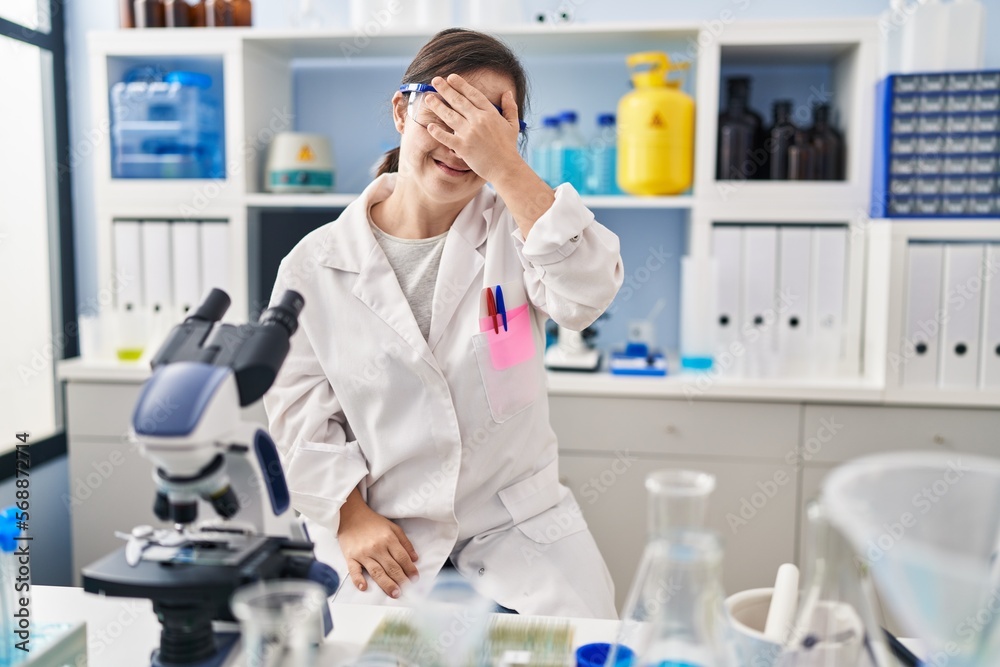 Hispanic girl with down syndrome working at scientist laboratory covering eyes with hand, looking serious and sad. sightless, hiding and rejection concept Hispanic girl with down syndrome working at scientist laboratory covering eyes with hand, looking serious and sad. sightless, hiding and rejection concept