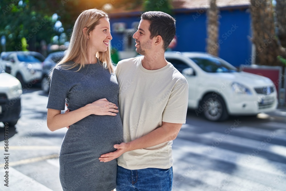 Man and woman couple standing together touching belly at street