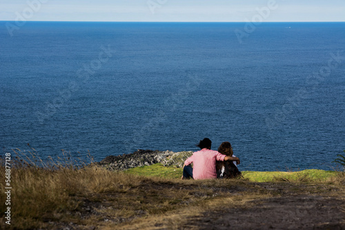 View from behind of a young couple sitting on the floor watching the sea