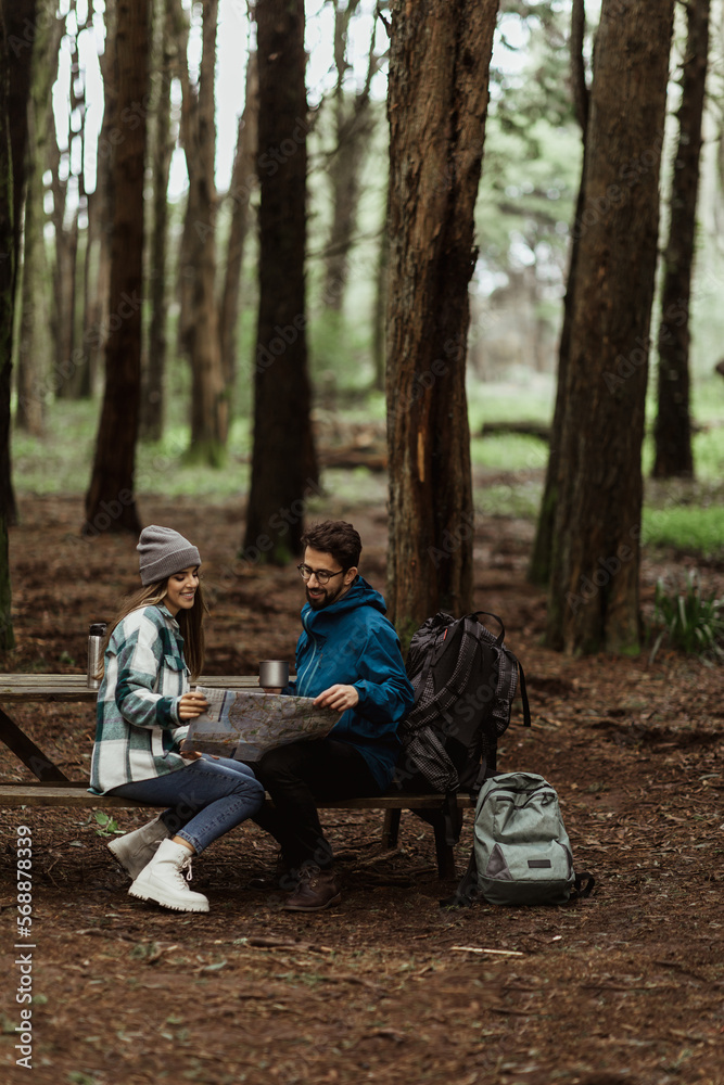 Glad young european man and lady tourists in jackets with backpack resting in forest, enjoy cold season outdoors