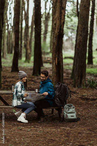 Glad young european man and lady tourists in jackets with backpack resting in forest, enjoy cold season outdoors