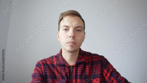 A young man in a red shirt looks at a laptop screen during a video meeting. A man drinks water from a clear glass. View from the laptop camera. High quality 4k footage