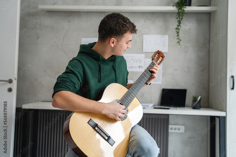 Obraz premium One young man Caucasian teenager sit at home in room playing guitar