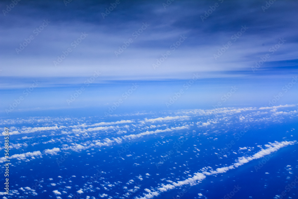 Cloudscape background. View from above, out of an airplane window. Different shades of blue in the sky.