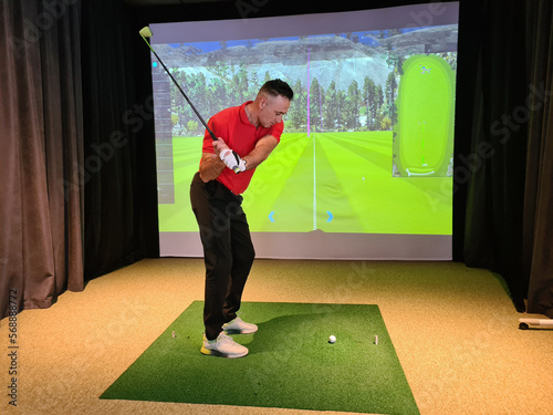 Professional male golfer holding club playing golf indoors on golf simulator photo
