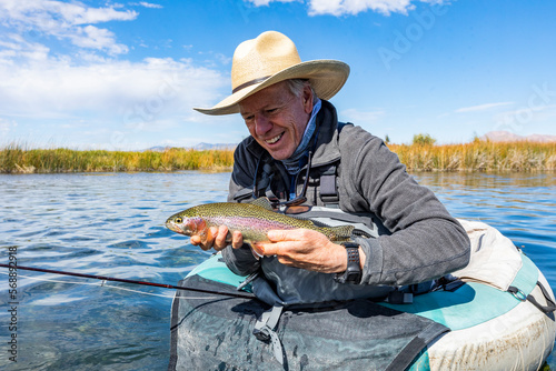Senior fly fisherman holds rainbow trout before releasing back into spring creek photo