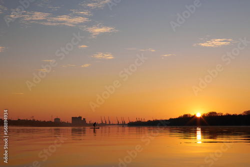 Silhouette of a woman rowing on stand up paddle board (SUP) board at sunrise through the shiny water surface of river