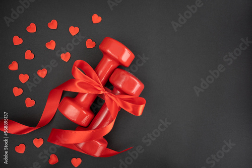 Gym dumbbells wrapped in red ribbon as a love gift for Valentine's Day, marriage proposal engagement, anniversary or wedding. Fitness workout and sport training flat lay composition with copy space.