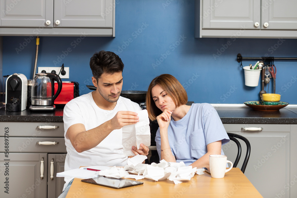 Family financial crisis concept. Shocked and stressed couple counting expenses, taxes and debts. Laptop and many bills on the table Family financial crisis concept. Shocked and stressed couple counting expenses, taxes and debts. Laptop and many bills on the table