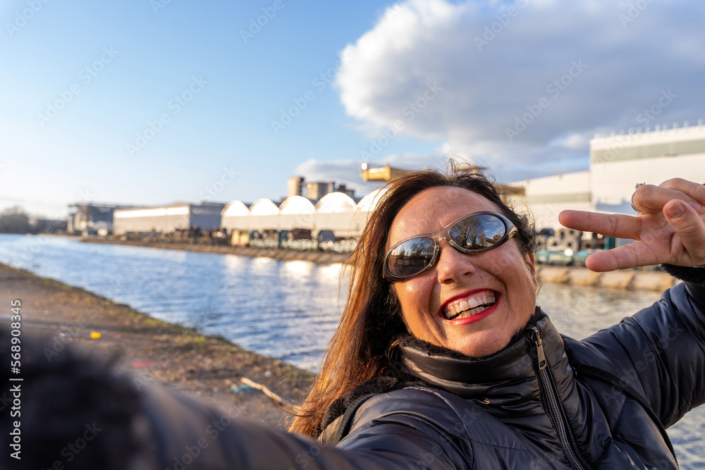 middle aged woman wearing winter clothes taking a selfie by a river
