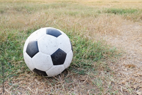 An old dirty ball on green and dried brown grass field in outdoor space 