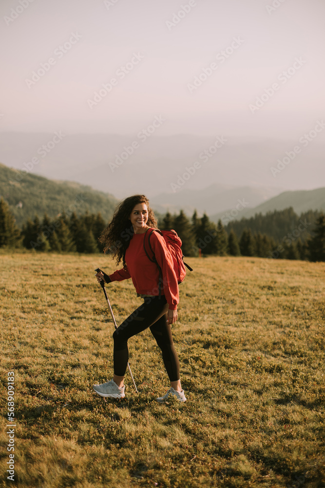 Young woman is taking a scenic hike on a hill, carrying all her necessary gear in a backpack Young woman is taking a scenic hike on a hill, carrying all her necessary gear in a backpack