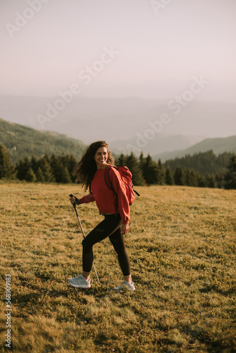 Young woman is taking a scenic hike on a hill, carrying all her necessary gear in a backpack