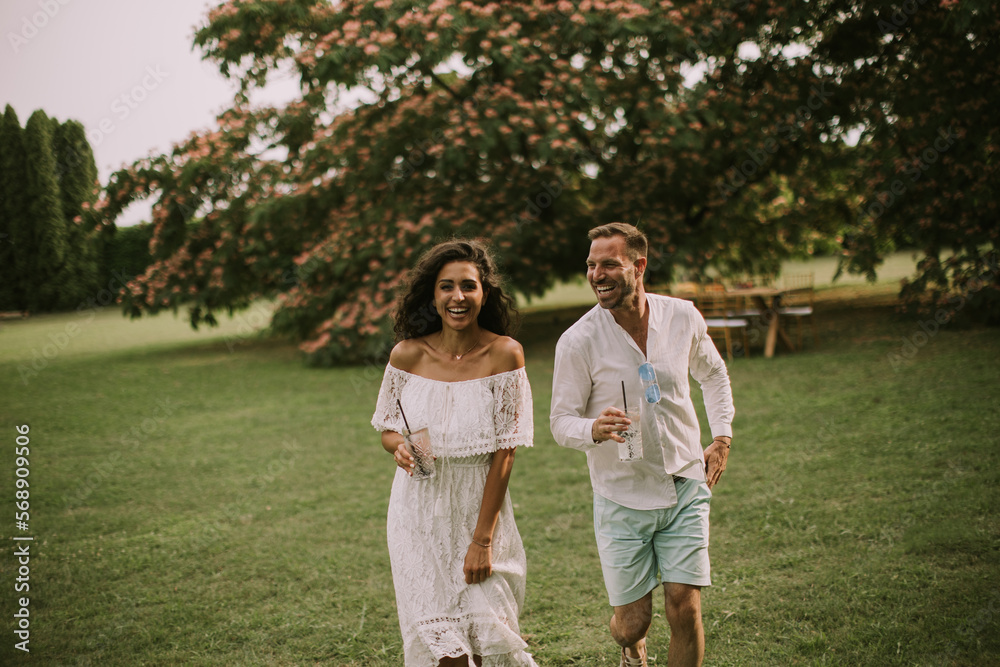 A happy young couple is enjoying the beautiful surroundings of a garden with glasses of fresh lemonade A happy young couple is enjoying the beautiful surroundings of a garden with glasses of fresh lemonade