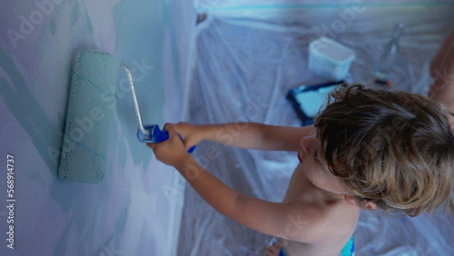 Child painting wall with paint roller. Adorable small boy paints with equipment. Kid helping parent with house renovation