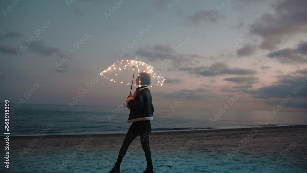 Pretty model girl on the night beach with a magic glowing umbrella 