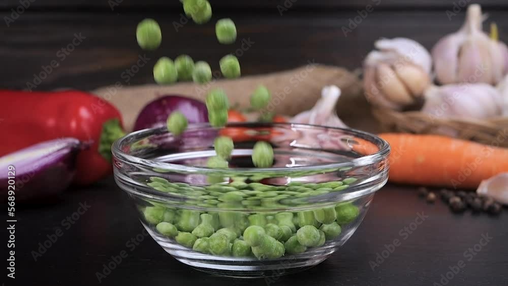 Frozen peas falling into a glass bowl with vegetables in background