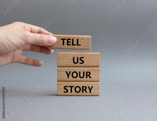 Tell us your story symbol. Concept words Tell us your story on wooden blocks. Beautiful grey background. Businessman hand. Business and Tell us your story concept. Copy space.