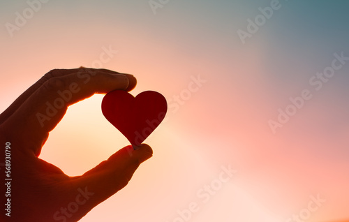 Hand holding heart on colorful sky background 