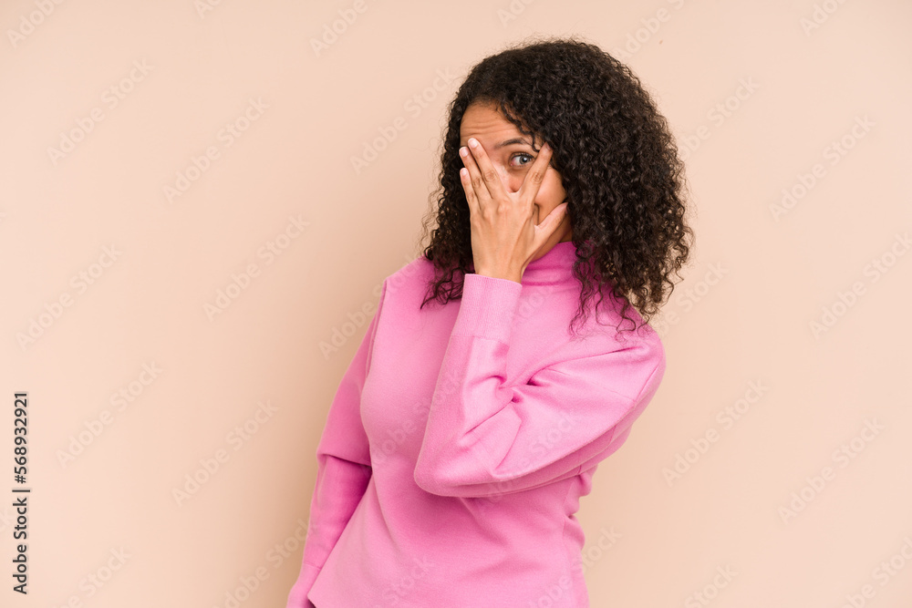 Young african american curly woman isolated blink at the camera through fingers, embarrassed covering face. Young african american curly woman isolated blink at the camera through fingers, embarrassed covering face.