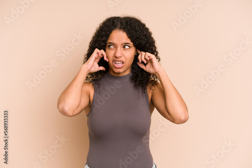 Young african american curly woman isolated covering ears with fingers  stressed and desperate by a loudly ambient.