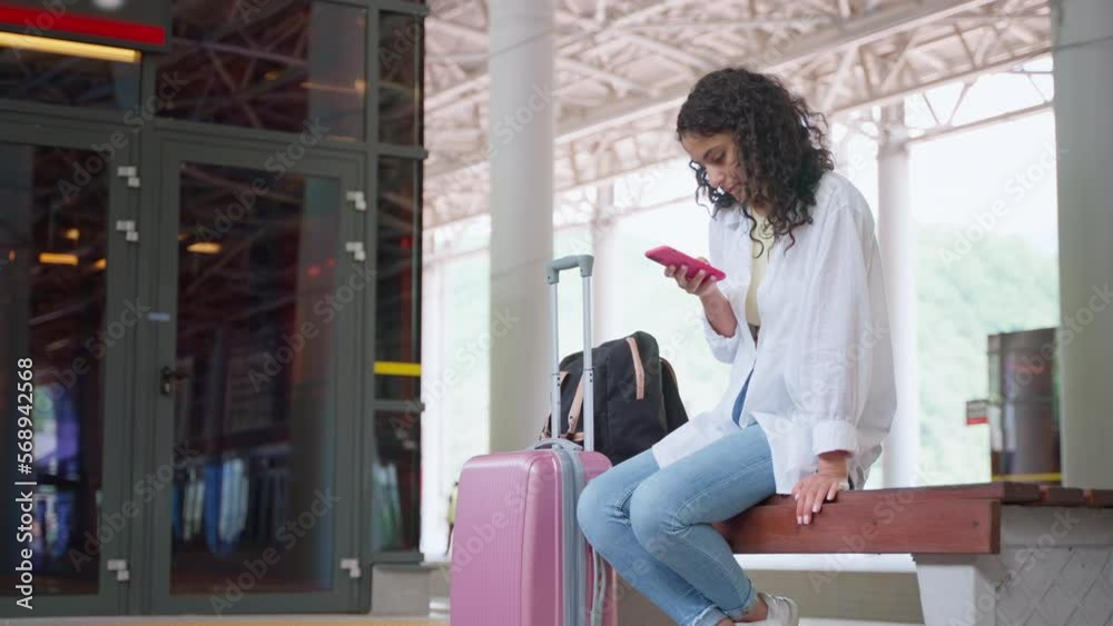 alone woman passenger on empty platform of suburban trains, sitting on bench, using smartphone alone woman passenger on empty platform of suburban trains, sitting on bench, using smartphone