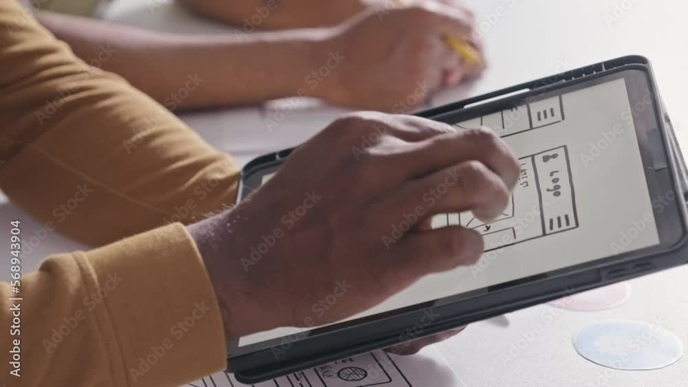 Close up shot of hands of UX designer discussing mockup of mobile app interface on digital tablet with colleagues while cooperating in office