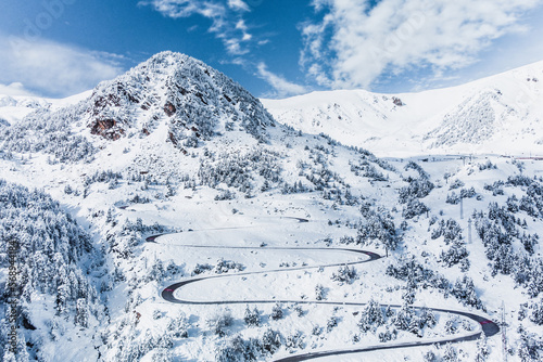 Vallter 2000 ski resort and snowy peak of Gra de Fajol mountain.Winter landscape with winding road, snowy mountains and trees covered with snow. Setcases, Ripollés, Girona Pyrenees, Catalonia.