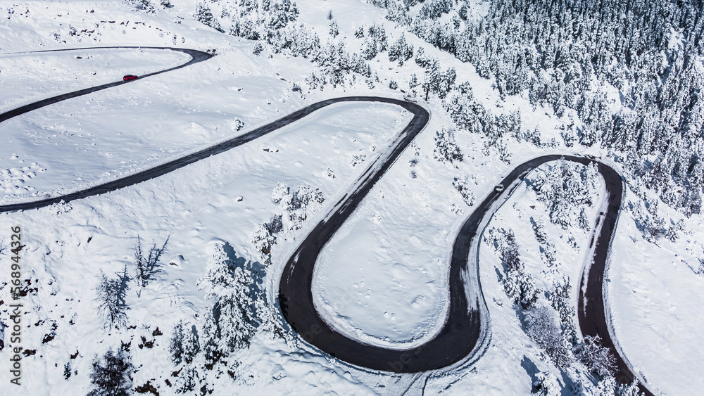 Winding road in a winter landscape of a mountain pass. Windy curvy road covered with snow. Vacations, travel, drive, route, journey and tourism concept.