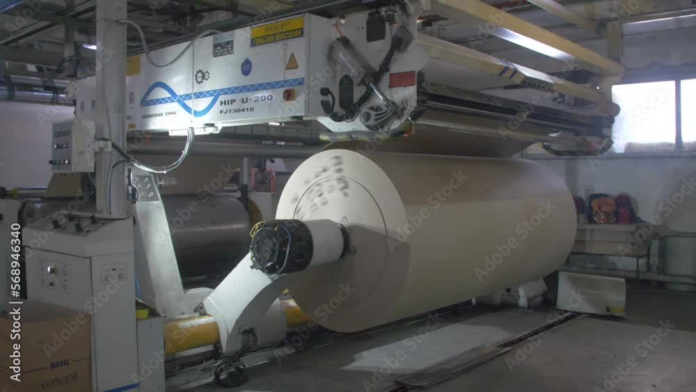 Huge roll of packaging paper rotates on a modern machine in the cardboard production hall Huge roll of packaging paper rotates on a modern machine in the cardboard production hall