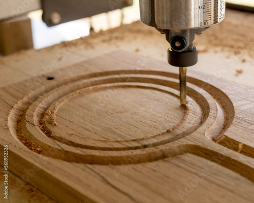 A CNC machine routing a circle on an oak wood board