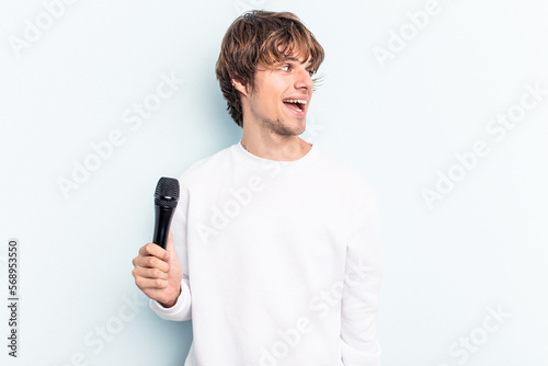 Young caucasian singer man isolated on blue background looks aside smiling, cheerful and pleasant.