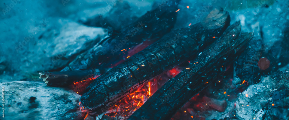 Vivid smoldered firewoods burned in fire close-up. Atmospheric warm background with orange flame of campfire and blue smoke. Full frame image of bonfire. Beautiful whirlwind of embers and ashes in air Vivid smoldered firewoods burned in fire close-up. Atmospheric warm background with orange flame of campfire and blue smoke. Full frame image of bonfire. Beautiful whirlwind of embers and ashes in air