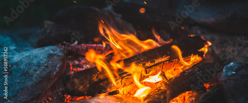 Vivid smoldered firewoods burned in fire close-up. Atmospheric warm background with orange flame of campfire. Unimaginable full frame image of bonfire. Burning logs in beautiful fire. Wonderful flame.