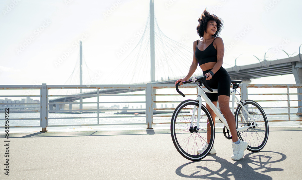 Fototapeta premium Ecological transport for every day. Healthy lifestyle, A woman smiling curly hair in sportswear walking on a white bicycle.