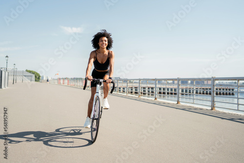 Fototapeta A young woman with curly hair in sports clothes riding a bicycle in the city