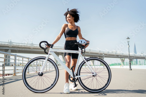 A woman smiling curly hair in sportswear riding a white bike in the city. Ecological transport for every day.
