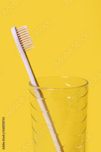 Ecological bamboo toothbrush in a glass cup on a yellow background. Oral hygiene care concept. Environmentally friendly wooden toothbrush