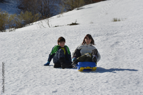 Mujer sentada en un trineo azul y un niño sentado en la nieve