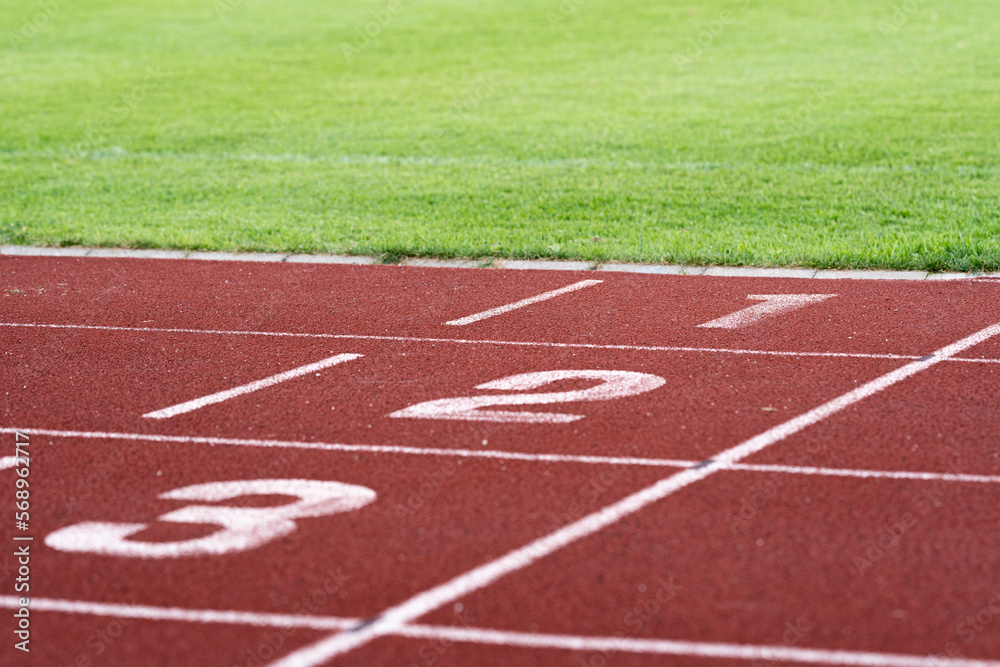 Red running racetrack finishing line with numbers 1-3. Green grass. Landscape or horizontal photo.