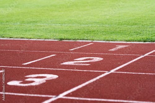 Red running racetrack finishing line with numbers 1-3. Green grass. Landscape or horizontal photo. © AnnaKoo