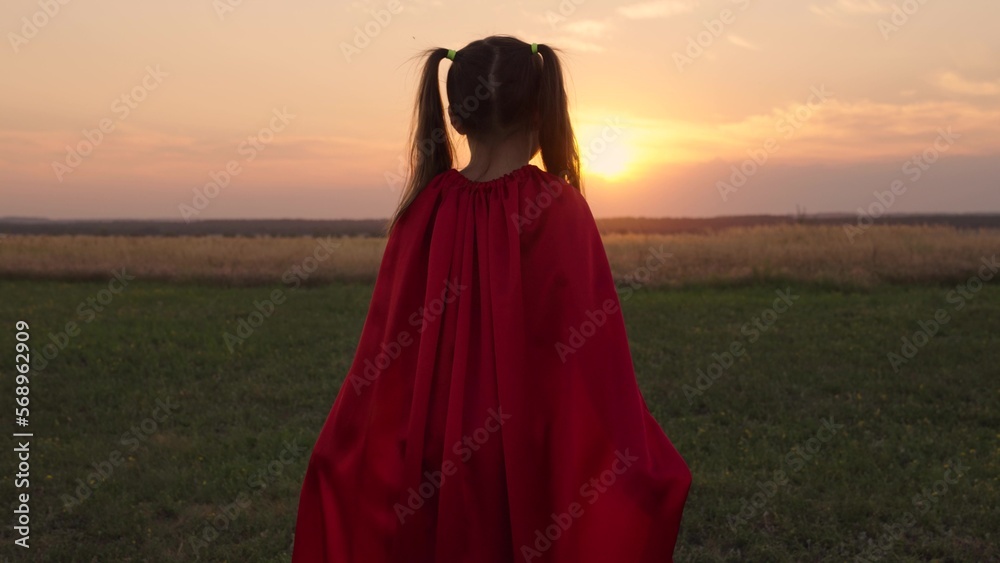 Active child girl superhero runs at sunset in field. Silhouette of child superhero in park. Winner daughter in red raincoat in sunny park, happy childhood. Concept of victory, success. Chidhood dream