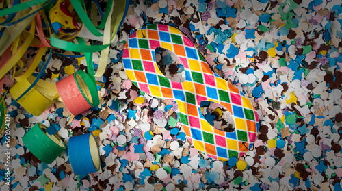 Carnival themed background with Harlequin mask over confetti, buglers and streamers