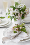 Beautiful table decor for a wedding dinner with a spring blooming apple tree flowers. Celebration of a special holiday marriage event. Fancy white plates, wineglasses