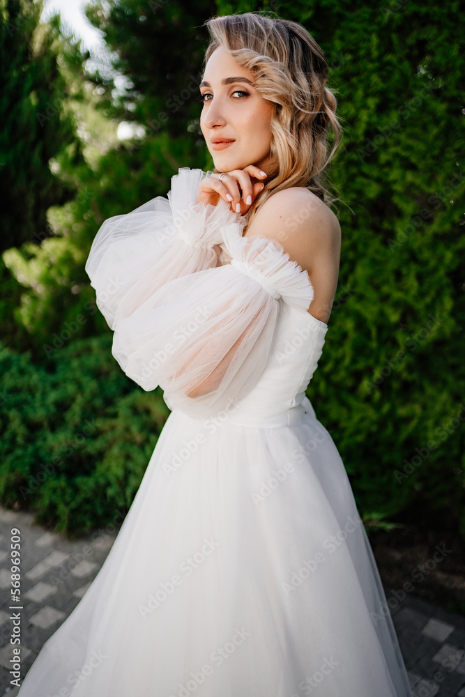 a bride in an open-shouldered dress poses against the backdrop of greenery a bride in an open-shouldered dress poses against the backdrop of greenery
