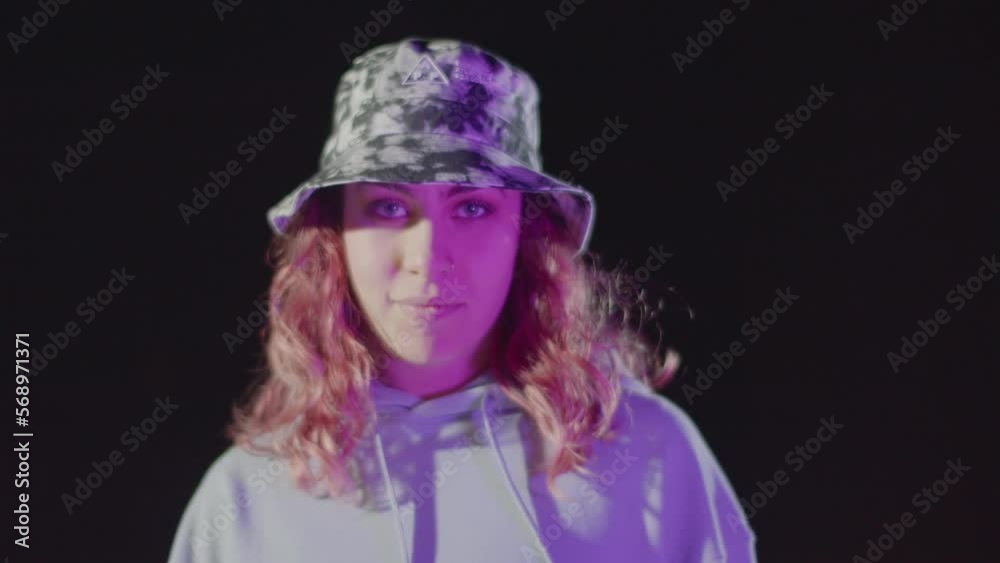 Portrait shot of pretty red-haired young lady looking at camera while making rhythmic dance moves against dark background. Female dancer in camouflage hat smiling mysteriously. Attitude, youth concept Portrait shot of pretty red-haired young lady looking at camera while making rhythmic dance moves against dark background. Female dancer in camouflage hat smiling mysteriously. Attitude, youth concept