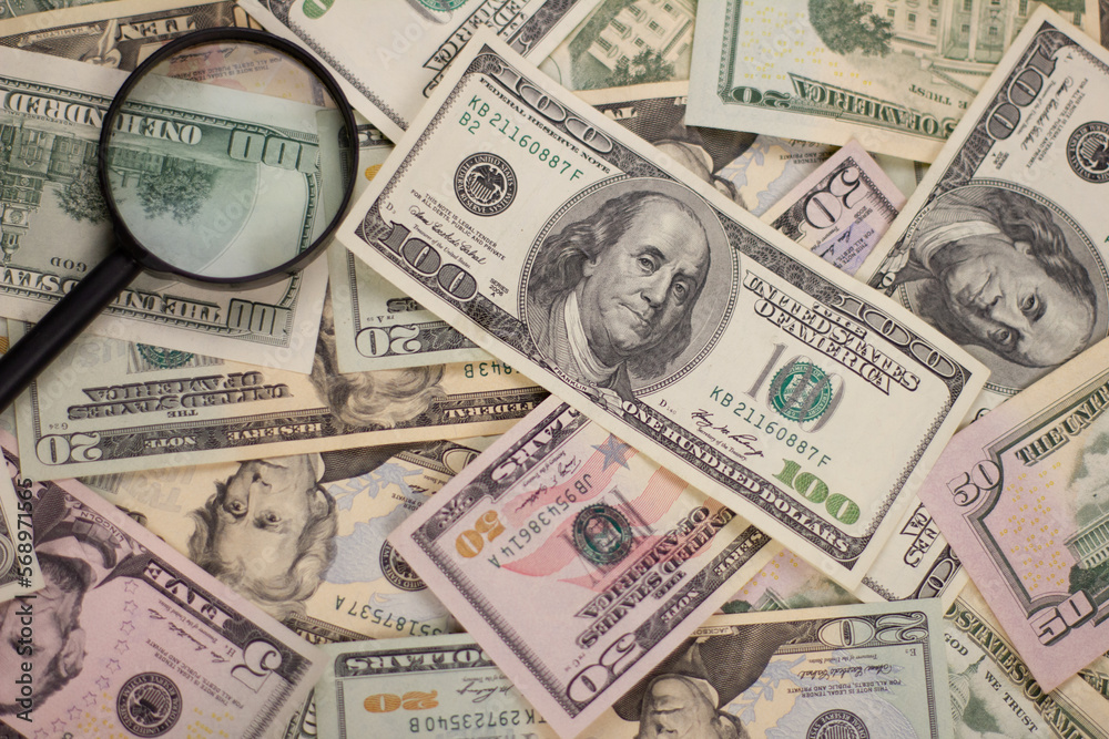 Background from dollars of different values. On top of dollar bills lies a paw in the corner. The concept of money and authentication with a magnifying glass. Background from dollars of different values. On top of dollar bills lies a paw in the corner. The concept of money and authentication with a magnifying glass.